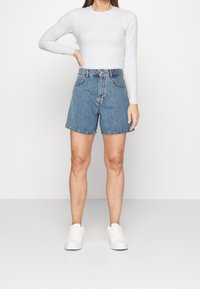 Shorts de mezclilla de cintura alta, color azul claro, con dobladillo deshilachado y dos bolsillos laterales; combinados con una camiseta gris de manga larga y zapatillas blancas.