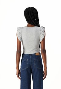 Top gri cu mânecă scurtă, cu nervuri și umeri volan, asortat cu blugi din denim albastru închis cu talie înaltă, având buzunare pe spate și o etichetă din piele.