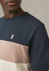 Bomuld T-shirt med en marineblå øverste del og en beige-grå nederste del, med et lille broderet logo og rund halsudskæring.
