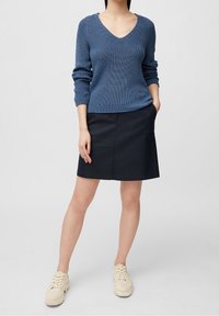 Un pull en tricot bleu avec un col en V et des manches longues, associé à une jupe sombre et des baskets beiges. L'ensemble présente une coupe décontractée et une texture agréable.