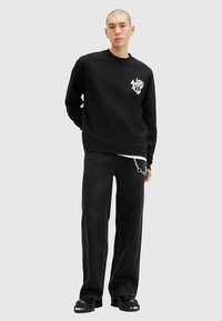 Felpa nera con scollo rotondo, caratterizzata da una grafica bianca sul petto. Abbinata a jeans neri larghi e scarpe nere chunky.