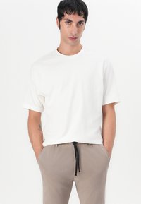 Tricou alb texturat cu manșete scurte și guler rotund, asociat cu pantaloni scurți, cu șnur în nuanță de maro deschis. Croială relaxată, design simplu.