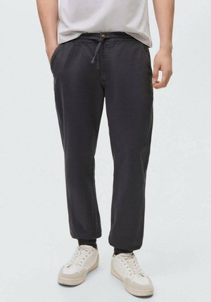 Pantaloni jogger grigi scuri con vita elastica, cordino e caviglie a costine; realizzati in tessuto morbido; abbinati a sneaker bianche.