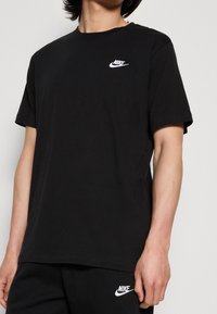 Černé bavlněné tričko s kulatým výstřihem, krátkými rukávy a bílým logem Nike na levé straně hrudi. Hladká textura, volný střih.