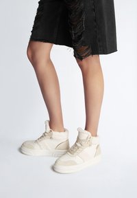 Sneaker alte bianche con fodera in pelliccia sintetica, dettagli in camoscio e pelle, e colletto imbottito. La suola è testurizzata per una presa migliore.