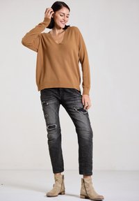 Brown v-neck sweater, gray distressed jeans with rips, and beige ankle boots. Soft texture, relaxed fit, and casual style.