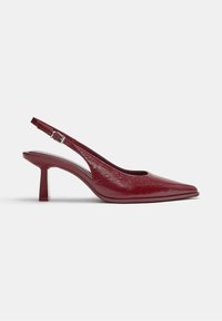 Chaussure slingback en cuir rouge à bout pointu, talon bloc de hauteur moyenne et bride ajustable avec boucle argentée, présentée sur fond blanc.