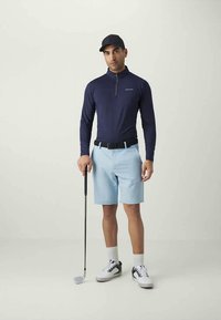 Mornarsko modra majica z dolgimi rokavi in zadrgo za golf ter svetlo modre kratke hlače. Črni pas, bele nogavice in črno-bele golf čevlje. Drži golf palico.