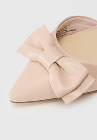 Γωνιακό παπούτσι με μακρύ δάκτυλο από μαλακό μπεζ δέρμα με μια μεγάλη ομαλή λεπτομέρεια φιόγκου. Διαθέτει επίπεδη σόλα και ρουζ εσωτερική επένδυση.