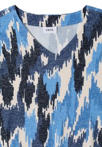 Haut à manches courtes et col en V de couleur crème, présentant un motif abstrait bleu et noir. Fabriqué en tissu doux et texturé. Étiquette de la marque : CECIL.