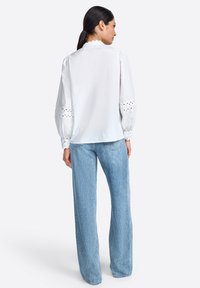 Blouse blanche à manches bouffantes, décolleté festonné et détails en broderie anglaise sur les poignets, associée à un jean large bleu clair.