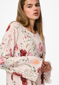 Majica dugih rukava s cvjetnim uzorkom i naboranom teksturom, svijetlo ružičasta pozadina i širom rukavi s raznim bojama i uzorcima cvijeća.