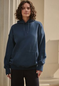 Marineblauer Baumwoll-Hoodie mit einer Fronttasche, langen Ärmeln, einem Kapuzenzug und einem lässigen Schnitt. Schlichtes Design mit gerippten Bündchen und Saum.