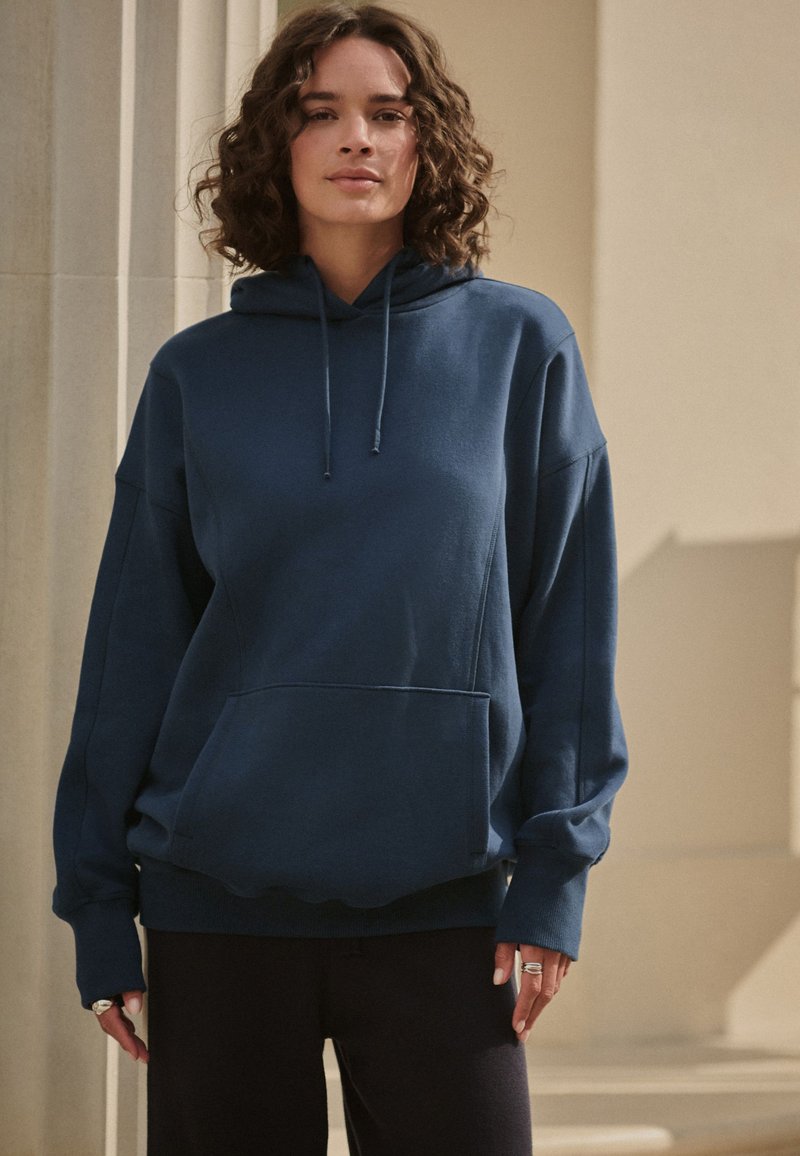 Marineblauer Baumwoll-Hoodie mit einer Fronttasche, langen Ärmeln, einem Kapuzenzug und einem lässigen Schnitt. Schlichtes Design mit gerippten Bündchen und Saum.