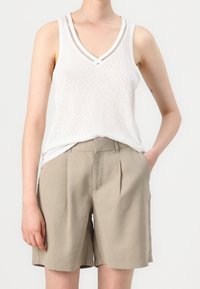 Bílý bezrukávový top s výstřihem ve tvaru V a texturovanou tkaninou, doplněný khaki šortkami s vysokým pasem a sklady.