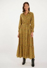 Robe longue à boutons avec une base jaune et un motif floral en vert et rouge. Elle a une taille cintrée et une jupe à volants.