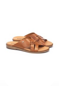 Sandalias de piel marrón con diseño de tiras cruzadas, textura suave y suela de goma. El detalle de acento incluye un pequeño botón decorativo.