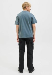 T-shirt grigio a maniche corte in cotone, abbinato a pantaloni cargo neri con tasche laterali e vestibilità rilassata, visto da dietro.