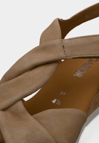 Μπεζ σουέντ σανδάλι με στριφτό σχέδιο λουριού και ανοιχτό δάχτυλο. Η εσωτερική σόλα δείχνει το μέγεθος και τα στοιχεία της μάρκας. Υφασμένη πάτος για άνεση.