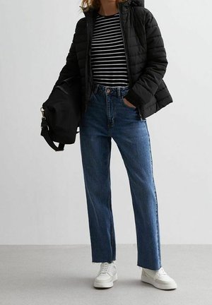 Czarna kurtka puchowa, koszula z długim rękawem w paski, jeansy w kolorze niebieskim o wysokim stanie i prostym kroju oraz białe trampki. Czarna torba po boku.