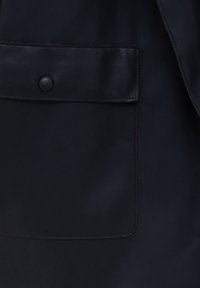 Pochette en cuir noir avec bords cousus et un seul bouton-pression rond noir sur un fond en tissu foncé.