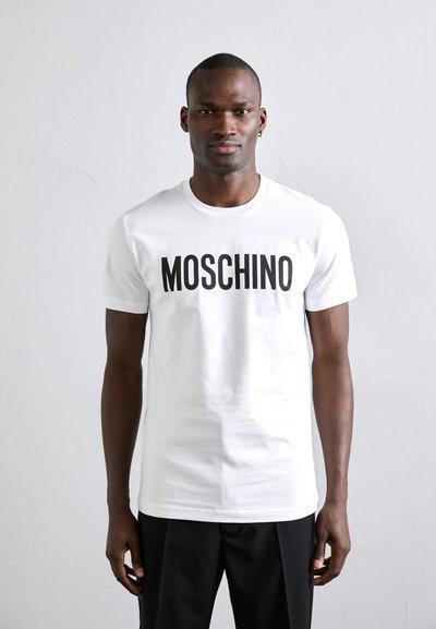 Fehér pamut póló, elöl feltűnő fekete "MOSCHINO" felirattal. Rövid ujjú, kerek nyakú, szabványos fazon. Egyszerű dizájn.