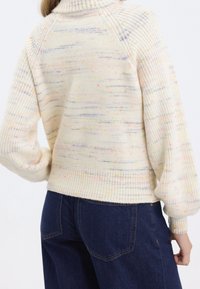 Pull en tricot avec col montant, base crème parsemée de taches multicolores, poignets et bord côtelés, coupe décontractée.