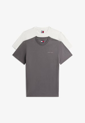 Dwie składane koszulki Tommy Jeans, jedna szara z logo na piersi, a druga biała, ułożone warstwowo z szarą koszulką z przodu na białym tle.