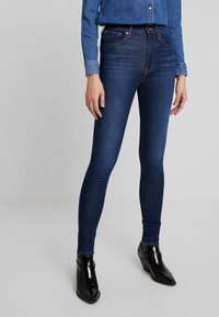 Tmavě modré skinny džíny vyrobené z denimu, s klasickým pětipocket designem a středním pasem, doplněné černými kotníkovými botami.