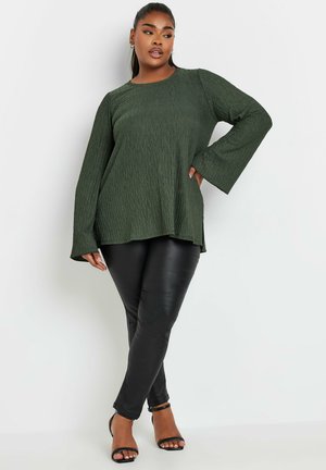 Dark green textured top with long sleeves paired with slim black leather-like pants and strappy black heels.