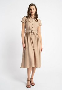 Beżowa sukienka midi z krótkimi rękawami, zapięcie na guziki z przodu, z paskiem w talii i zwiewnym dołem. Miękka tkanina o gładkiej fakturze. Sandały na obcasie.