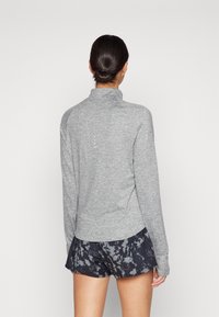 Grauer, langärmeliger Sportpullover mit hohem Kragen und flachen Nähten, kombiniert mit Shorts in Schwarz und Grau mit Muster. Weicher, leichter Stoff.