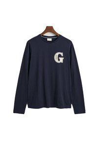 Námorně modré tričko s dlouhým rukávem vyrobené z bavlny. Na levé hrudi se nachází velké krémové logo "G" a má kulatý výstřih. Příjemně měkká textura.