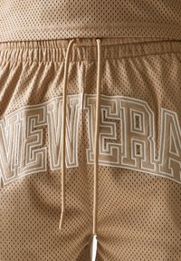 Μπεζ σορτς από δίχτυ διαθέτουν ελαστική μέση με κορδόνια, λευκό κεντημένο κείμενο "NEW ERA" στο πλάι και διαπνέον ύφασμα με οπές.