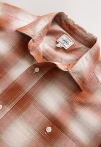 Camicia a quadri in toni arancioni e bianchi, con chiusura a bottoni, colletto classico e tessuto morbido. Vestibilità standard con etichette visibili.