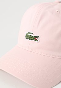 Casquette de baseball rose en coton. Dotée d'une visière incurvée et d'un logo de crocodile vert avec des accents rouges brodés sur le devant.