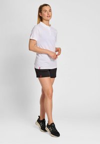 Biała koszulka polo z krótkim rękawem i kołnierzykiem, zestawiona z czarnymi szortami z czerwonymi akcentami. Czarne sportowe sneakersy dopełniają całość.