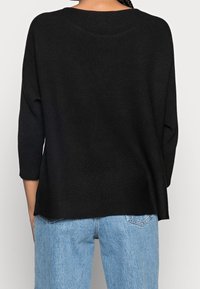 Maglione nero a coste con maniche a tre quarti, caratterizzato da una vestibilità rilassata e un orlo leggermente arrotondato. Abbinato a jeans di denim azzurro chiaro.