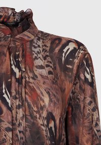 Long-sleeve blouse in lightweight, semi-sheer fabric featuring a multi-patterned design of browns, black, and red with a high ruffled neckline.