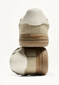 Beige Sneaker mit einem weichen Lederoberteil, kontrastierendem weißen Absatz und Gummisohle mit horizontalen Rillen. Abgerundete Zehenform.