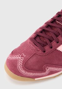 Bordoopunane seemisnahast king roosa tikandiga, ümar nina ja sobivate paeladega. Omaduseks on tekstureeritud kummist tald haarduvuse tagamiseks.