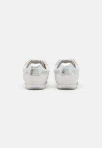 Hvite sneakers med en glatt skinn-overdel, metalliske detaljer på hælen, teksturert såle og merkevarelogo på baksiden. Minimalistisk design.