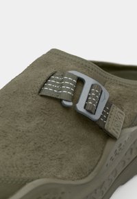 Πράσινο σουέτ παπούτσι χωρίς κορδόνια με μεταλλική πόρπη και υφασμάτινη σόλα από καουτσούκ με μικρές εγκοπές για αερισμό.