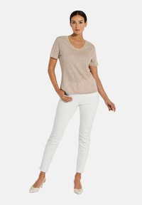 Beige V-Ausschnitt-T-Shirt mit kurzen Ärmeln, weicher Textur, kombiniert mit weißen, eng anliegenden Hosen und hellbeigen Schuhen. Einfaches Design, minimalistische Akzente.