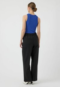 Blauwe geribbelde tanktop gecombineerd met zwarte wijde broek met elastische tailleband en zijzakken, model van achteren gezien.