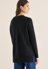 Černý svetr s volným střihem, žebrovaným lemem a bočními rozparky. Měkká textura a dlouhé rukávy, zobrazen z lehce otočeného zadního pohledu.