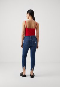 Κόκκινη καλοκαιρινή μπλούζα με τιράντες συνδυασμένη με εφαρμοστά μπλε τζιν που έχουν φθαρμένα τελειώματα και δύο πίσω τσέπες, συμπληρωμένη από μαύρα υποδήματα.