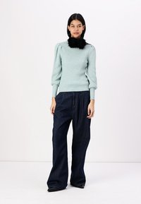 Light blue ribbed sweater with puff sleeves, featuring a black faux fur collar. Paired with wide-leg dark blue denim jeans.