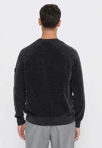 Maglione grigio scuro con schiena strutturata, polsini e cintura a costine. Presenta un design semplice e una vestibilità comoda, adatto per un abbigliamento casual.