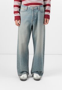 Jean large bleu clair avec un aspect délavé, présentant une fermeture à bouton et à glissière, cinq poches et une texture légèrement usée.
